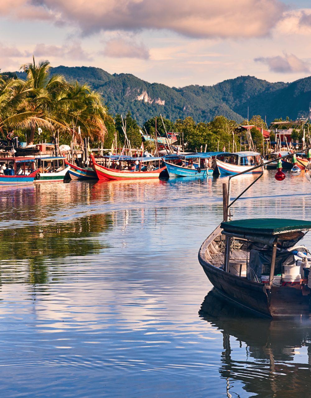 A local fisherman goes out on a boat from boats park to the sea for fishing. Traditional colorful asian fishing boats in fishing village. Langkawi island, Malaysia.